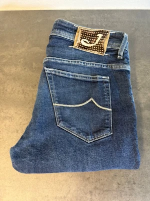 Blå  jeans från Jacob Cohen W34 - Snygga blå jeans från Jacob Cohen med smal passform och klassisk femficksdesign. Jeansen har kontrastsömmar och ett unikt märke med J på bakfickan. Tillverkade i mjuk denim med stretch för extra komfort.