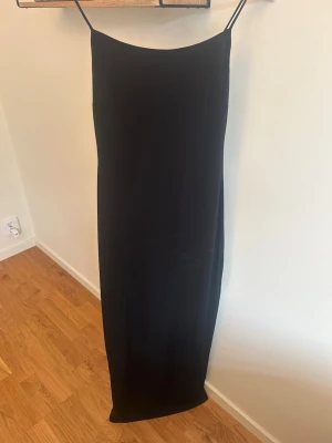 Svart lång klänning  - Stilren svart långklänning från bikbok  med tunna axelband och rak passform. Klänningen har en minimalistisk design och är perfekt för dig som gillar enkelhet. Tillverkad i mjuk polyester som ger ett snyggt fall.