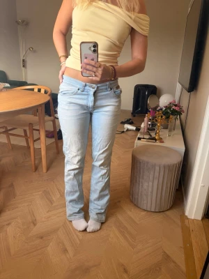 Lågmidjade Ljusblå bootcut jeans - Säljer ett par ljusblå bootcut jeans med låg midja och klassisk femficksdesign. Jeansen har en avslappnad passform och är tillverkade i denim med lätt tvättad look. Perfekta för en trendig och avslappnad stil. Lite slitna längst ned då dem är för långa för mig. Storlek W29 L32 jag är 163 för referens 