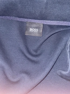 Mörkblå hoodie från Hugo Boss - Snygg mörkblå hoodie från Hugo Boss med dragkedja och diskret logga på ärmen. Tillverkad i mjukt material som känns skönt mot huden. Perfekt för en avslappnad och stilren look.