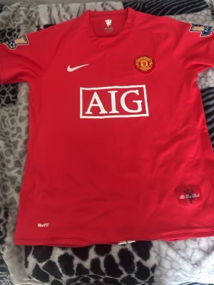 Manchester United Ronaldo matchtröja - Säljer en klassisk röd Manchester United matchtröja från Nike med AIG som sponsor, klubbmärke på bröstet och Premier League-patch på ärmarna. På ryggen står det Ronaldo och nummer 7. Tillverkad i lätt och ventilerande material, perfekt för fotbollsträning eller samling.
