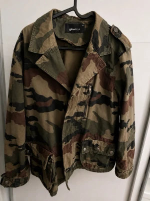 Camouflage parkajacka från Gina Tricot - Snygg camouflagefärgad parkajacka från Gina Tricot med klassisk krage, dragkedja och knappar. Jackan har flera fickor och justerbar midja. Perfekt för dig som gillar streetstyle och vill sticka ut lite extra.. Använd knappt, i mycket bra skick.
