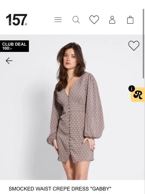 Brun prickig kortklänning Gabby - Kort brun klänning från 157 med vita prickar, v-ringning och långa puffärmar. Klänningen har smockad midja och knappar framtill, samt en liten slits nedtill. Perfekt för dig som gillar en söt och trendig look. aldrig använd då den var för liten så helt nyskick