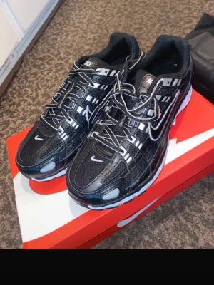 Nike svartvita sneakers med mesh - Svarta sneakers från Nike med vita detaljer och reflekterande inslag. Ovandelen är i mesh och syntet med tydliga sömmar och en stor vit Swoosh på sidan. Sulan är vit med svarta partier och skon har en sportig, modern look. Perfekta för dig som gillar streetwear.