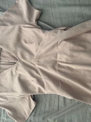 Beige topp med knyt i midjan - Säljer en stilren beige topp med v-ringning och korta ärmar. Klänningen har ett snyggt knyt i midjan och dragkedja i ryggen för enkel påklädning. Perfekt för dig som gillar minimalistisk och modern stil.