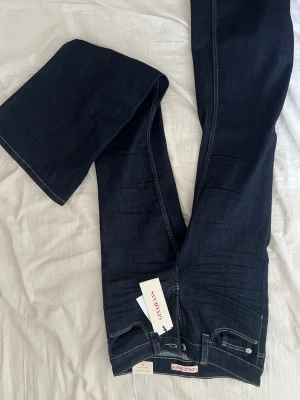 Mörkblå bootcut jeans GINA - Säljer ett par mörkblå bootcut jeans från GINA med klassisk femficksmodell och kontrastsömmar. Jeansen har en snygg utsvängd passform och är tillverkade i ett mjukt denimtyg. Perfekta för dig som gillar tidlös och stilren look.