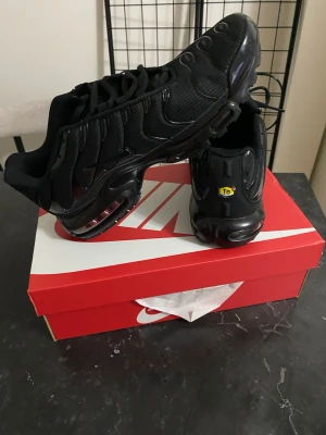 Nike Air Max Tn  Plus helsvarta sneakers - Säljer ett par helsvarta Nike Air Max Plus sneakers med ikoniska vågmönster och Tn-detalj på hälen. Skorna har en chunky sula med synlig Air-enhet och är tillverkade i mesh och syntetmaterial. Perfekta för dig som gillar streetwear och vill ha en clean look.