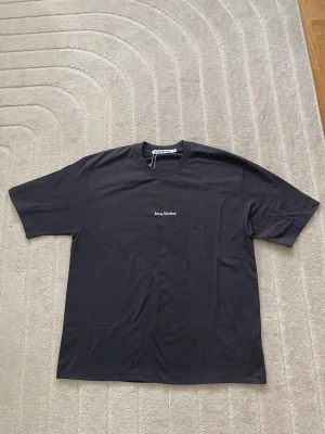 Svart Acne Studios t-shirt - Snygg svart t-shirt från Acne Studios med klassisk rund hals och diskret logga broderad i vitt på bröstet. Tillverkad i mjuk bomull och har en normal passform. Perfekt basplagg för en clean och stilren look.