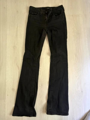 Svarta bootcut jeans från True religion.  - Säljer ett par svarta bootcut jeans från True religion med klassisk femficksmodell och knappgylf. Jeansen har bakfickor med lock och knapp, samt en snygg passform som sitter tajt upptill och släpper ut vid benen. Perfekta för en trendig och avslappnad look.