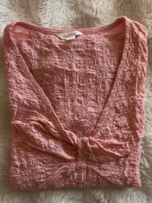 Topp - Supersöt rosa topp från Dobber med omlottdesign och knut framtill. Toppen har korta ärmar, v-ringning och är gjord i ett luftigt bomullstyg med struktur. Perfekt för dig som gillar en feminin och trendig stil.