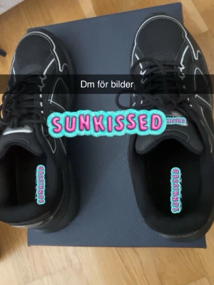 Svarta sneakers med vita detaljer - Snygga svarta sneakers med vita kontrastdetaljer och svarta skosnören. Ovandelen är i mesh och syntetmaterial för en sportig look. Sulan är svart och ger bra stöd. Perfekta för dig som gillar streetwear och vill ha en clean stil.