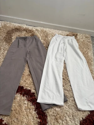 Två par mjukisbyxor, grå & vita - Säljer två par mjukisbyxor i basic stil, ett par i ljusgrått och ett par i vitt. Båda har resår i midjan och raka ben för en chill och avslappnad vibe. Perfekta för att hänga hemma eller dra till skolan i. Materialet känns mjukt och bekvämt mot huden.