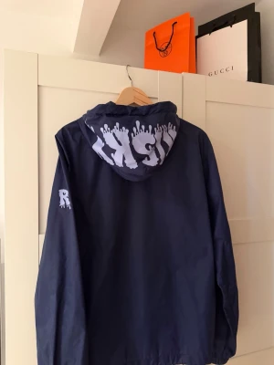 RISKY Blue Wind Jacket – M 🔥 - Navy blå vindjacka som vänder huvuden. Stor vit RISKY-print med dropp-effekt på insidan av huvan + matchande R på ärmen. Inuti sitter trigger warning-taggen: “People might get jealous… but f*ck em.” Lätt, skön och direkt street. Storlek M – sitter perfekt. Passar dig perfekt du som söker en vindjacka nu under våren samt sommaren den är i god skick.