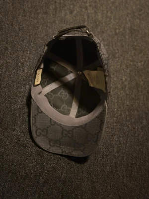 Svart Gucci keps med GG-mönster (sällsynt)  - Snygg svart keps från Gucci med det klassiska GG-monogrammet över hela kepsen. Justerbar rem baktill och böjd skärm. Tillverkad i slitstarkt tyg med exklusiv känsla och diskreta detaljer. Perfekt för dig som vill ha en stilren accessoar med lyxig touch. Knappast använd 