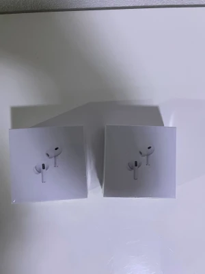 Apple AirPods Pro 2nd Gen MagSafe två st - Säljer två par Apple AirPods Pro 2nd Generation med MagSafe-laddningsetui. Trådlösa in-ear hörlurar i vit färg med stilren och kompakt design. Perfekta för musik, samtal och träning. Levereras i originalförpackning.