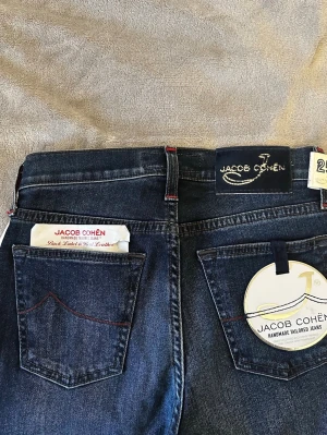 Mörkblå jeans från Jacob Cohën - Snygga mörkblå jeans från Jacob Cohën med klassisk femficksdesign och diskreta sömmar. Jeansen har en slim passform och patch i hästhår bak. Tillverkade i mjukt denimtyg för en bekväm känsla. Perfekta för dig som gillar stilrena och exklusiva jeans. W25, passar w26