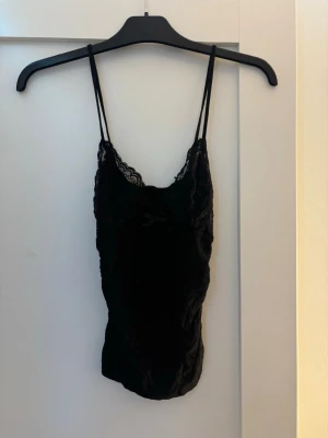 Svart spetslinne med tunna axelband - Säljer ett svart spets linne med tunna axelband och spetsdetaljer vid bysten. 