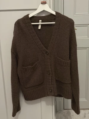 Brun kofta från kay/day med fickor - Mysig brun kofta från kay/day i storlek XS/S. Koftan har djup V-ringning, stora framfickor och knäppning med tre knappar. Tillverkad i mjukt stickat material och har ribbade muddar vid ärmslut och nederkant. Perfekt för lager på lager och chill stil. Har bara använt typ en gång