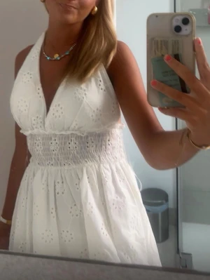 Vit broderad kort sommarklänning - Söt vit klänning med broderade blommor och omlott-v-ringning. Klänningen har smock i midjan och är ärmlös med halterneck. Köpt i Spanien förr förra året på en lokalbutik, så går nog inte att få tag på längre😁storlek one size men passar mig utmärkt som ofta har s/m i klänningar. Stretchigt material så passar nog även en storlek större. kan sälja för 199. 🥰