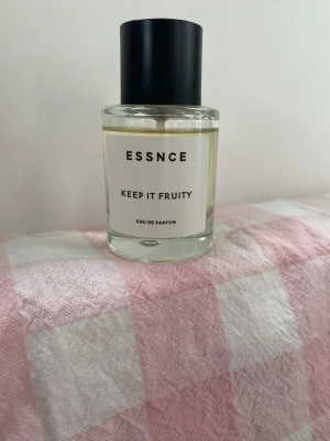 ESSNCE Keep It Fruity Eau de Parfum - Fräsch parfym från ESSNCE med namnet Keep It Fruity. Kommer i en rund, genomskinlig glasflaska med svart cylinderformad kork och enkel vit etikett. Doften är fruktig och modern, perfekt för dig som gillar lätta och fräscha parfymer. 