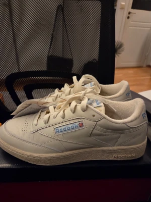 Reebok Club C 85 vita sneakers - Snygga vita Reebok Club C 85 sneakers med klassisk design och låg profil. Skorna är tillverkade i läder med Reebok-logga och brittiska flaggan på sidan. De har vita snören och en beige sula som ger en retro känsla. Endast testade alltså i nyskick. Kan absolut skicka fler bilder