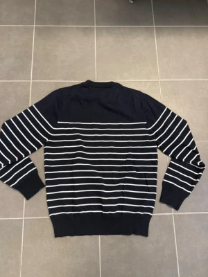 Marinblå stickad tröja med ränder - Snygg marinblå stickad tröja med vita horisontella ränder. Tröjan har rund halsringning och ribbade muddar vid ärmslut och nederkant. Perfekt för dig som gillar klassisk och stilren design. Pris går att diskutera!