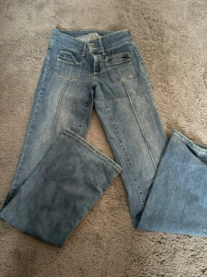 Blå utsvängda jeans med fickor - Snygga blå jeans med utsvängda ben. Jeansen har två stora fickor och en söm i mitten av byxan. Jeansen har ett litet hål som lätt går att sy ihop eftersom inget tyg har lossnat!