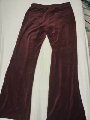 Vinröda mjukisbyxor i velour - Mysiga vinröda mjukisbyxor i mjuk velour med utsvängda ben och två bakfickor. Perfekta för chill dagar hemma eller när du vill ha en avslappnad stil. Resår i midjan för extra komfort.