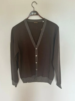 Brun kofta från Stenströms i merinoull - Snygg brun kofta från Stenströms med grå ribbade detaljer vid krage, knappslå och muddar. Koftan är tillverkad i 100% merinoull.