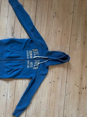 Vintage 2000s Blå zip hoodie från Hilfiger - En väldigt snygg och trendig vintage hoodie ifrån Tommy Hilfiger. Tröjan har lite slitningar längst ner och i ärmarna men det gör den bara snyggare! Om man letar efter tröjor i den stilen är denna i perfekt skick! Priset kan diskuteras.