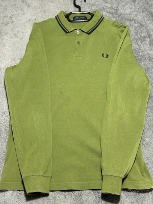 Fred Perry Long Sleeve Polo – Olive Green – Size M - Klassisk långärmad piké från Fred Perry i snygg olivgrön färg.  Stilren modell med broderad logga – perfekt för en mer uppklädd casual look.  Detaljer • Fred Perry • Långärmad piké • Olivgrön • Storlek M  📦 Snabb frakt 💬 Hör av dig vid frågor Se första bilden