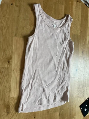 Ljusrosa linnetopp från 157 - Säljer en enkel och stilren ljusrosa linnetopp från 157. Toppen är ärmlös med rund halsringning och tillverkad i mjuk bomull, perfekt för varma dagar eller som lager under andra plagg.