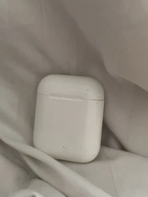 Vita trådlösa hörlurar med laddningsetui - Säljer ett par vita trådlösa Apple  hörlurar fodral  med laddningsetui. Etuiet är kompakt och har en rundad form med magnetlock och knapp på baksidan. Perfekt för dig som vill ha smidiga hörlurar till mobilen eller datorn.