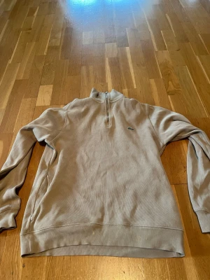Beige halfzip från Lacoste - Snygg beige halfzip-tröja från Lacoste små fläckar längst men inget som syns när du har på dig den billigare vid snabb affär