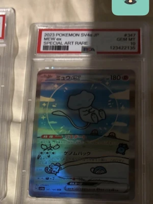 Pokémonkort Mew Charizard Och Umbreon - Japanskt Pokémonkort Mew ex från 2023, SV4a, Special Art Rare. Kortet är graderat av PSA med betyget GEM MT 10 och har en holografisk yta med färgglada detaljer och motiv av Mew. Flera kort