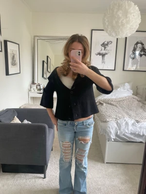 Svart stickad kofta med 3/4 ärmar - Säljer en svart stickad kofta med bred ribbad krage och trekvartsärmar. Koftan har knäppning framtill med stora knappar och en avslappnad, lite boxig passform. Perfekt att slänga över en topp för en cool och chill look. Skriv om ni har frågor!💕