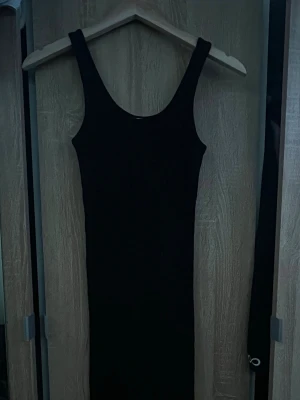 Svart ärmlös klänning XS från H&M - En enkel och stilren svart klänning i figurnära modell. Klänningen är ärmlös med breda axelband och har en rak, lång siluett. Perfekt för dig som gillar minimalistisk stil och vill ha en klassiker i garderoben. Använt 1 gång 