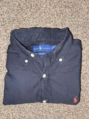 Svart skjorta från Ralph Lauren - Klassisk svart skjorta från Ralph Lauren. Använd näst intill 1-2 gånger. 10-10 skick men skulle behöva strykas. Inga defekter.