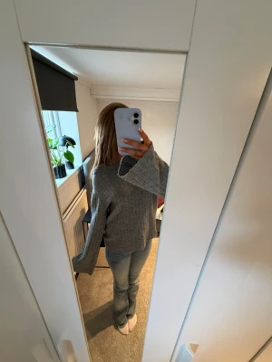 Grå stickad tröja med vida ärmar - Säljer en grå stickad tröja med ribbad struktur och vida, långa ärmar. Tröjan har en avslappnad passform och är perfekt för kyliga dagar. Passar till jeans eller kjol för en enkel och snygg look.