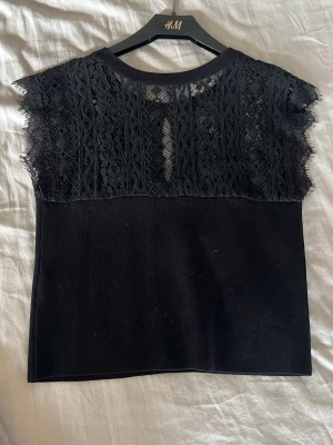 Svart spetsblus från H&M - Snygg svart blus med spetsdetaljer över axlar och bröst. Blusen har rund halsringning och är ärmlös med vackert mönstrad spets upptill. Perfekt för dig som gillar en feminin och trendig stil.