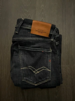 Mörkblå Replay Anbass - Snygga mörkblå jeans från Replay med raka ben och tydliga kontrastsömmar. Klassisk femficksmodell med läderpatch bak i midjan och diskret broderi på bakfickan. Tillverkade i slitstark denim som ger en cool look. Waist 30 length 33.