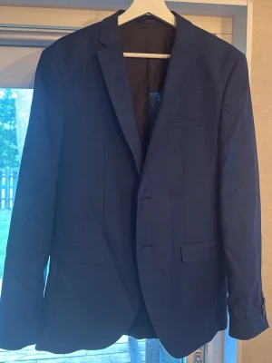 Mörkblå kavaj från Jack & Jones - Snygg mörkblå kavaj från Jack & Jones i super slim fit-modell. Klassisk design med två framfickor med lock, bröstficka och tvåknäppning. Fodrad insida med mönstrad innerficka. Perfekt för en stilren look. Nypris 600