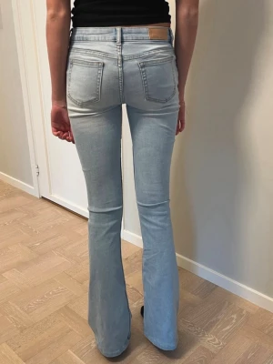 Bik bok jeans stl XS, 34 - Snygga ljusblå bootcut jeans med klassiska fem fickor och hög midja. Jeansen har en figurnära passform upptill och utsvängda ben. Tillverkade i stretchigt denimtyg för extra komfort. Perfekta för en trendig och avslappnad look.