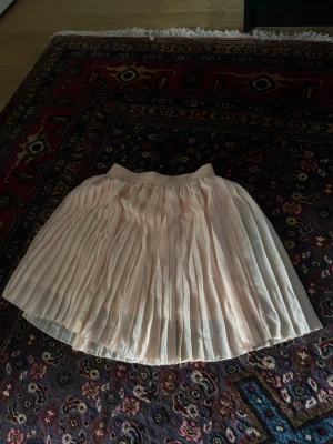 Ljusrosa plisserad kortkjol - Söt ljusrosa kortkjol med plisserad design och bred resår i midjan. Kjolen har ett skirt, luftigt tyg som ger en romantisk känsla och passar perfekt till vår och sommar. Enkel att matcha med både sneakers och sandaler. Nakd 