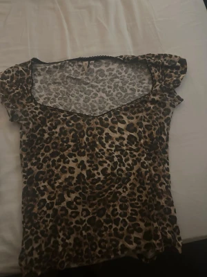 Leopardmönstrad topp från Nelly - Säljer en leopardmönstrad topp från Nelly med korta ärmar och v-ringad hals. Toppen har svarta spetsdetaljer längs halsringningen och är i ett mjukt, stretchigt material. Perfekt för dig som vill sticka ut lite extra.