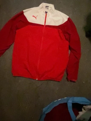 Puma Esito 3 leisure jacket - Snygg vindjacka från Puma i rött och vitt med dragkedja framtill och hög krage. Jackan har långa ärmar, två sidofickor och den klassiska Puma-loggan på bröstet. Perfekt för dig som gillar sportig stil och vill sticka ut.