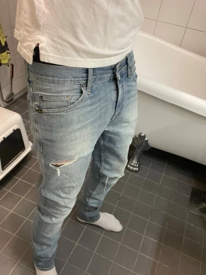 Ljusblå slitna jeans från Tiger of Sweden - Säljer ett par ljusblå jeans från Tiger of Sweden med skinny fit och slitningar på låret. Jeansen har klassisk femficksmodell, dragkedjegylf och läderpatch bak i midjan. Perfekta för en avslappnad och trendig look.