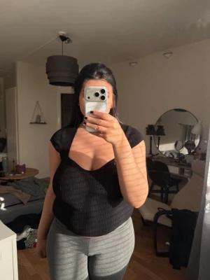 Svart ribbad croppad topp - Snygg svart croppad topp med ribbad struktur och breda axelband. Toppen har en unik skärning vid bysten som ger en modern look. Perfekt att styla med höga jeans eller kjol. Materialet känns mjukt och stretchigt. Den har ett litet hål men inget man lägger märke till 
