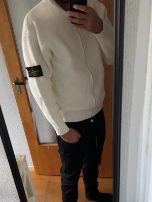 Vit ziptröja från Stone Island - Säljer en stilren vit ziptröja från Stone Island med ribbad struktur och klassisk logopatch på vänster ärm. Tröjan har hel dragkedja framtill och en avslappnad passform, perfekt för en clean och modern look. Använd max 4 gånger/ passar M och s/ personen på bilden är runt 180-183