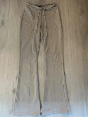Beige mjukisbyxor med utsvängda ben - Säljer ett par beige mjukisbyxor med utsvängda ben och dragsko i midjan. Byxorna har en mjuk och skön känsla, perfekta för chill dagar. Snygg söm längs benen för extra stilpoäng. Passar dig som gillar en relaxed och trendig look.